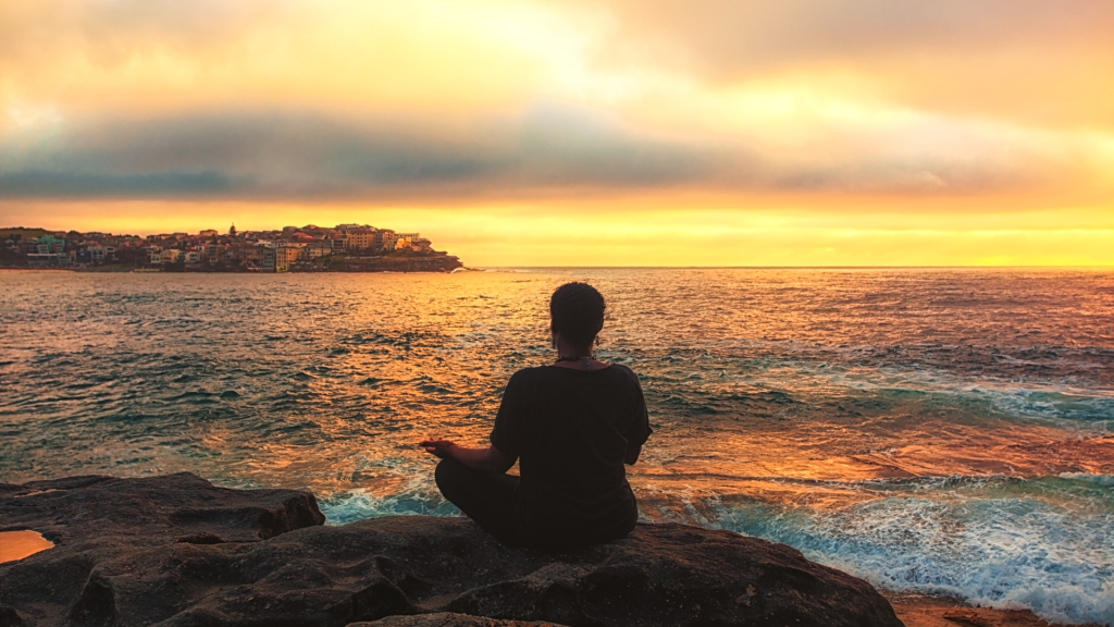 person meditating near the ocean